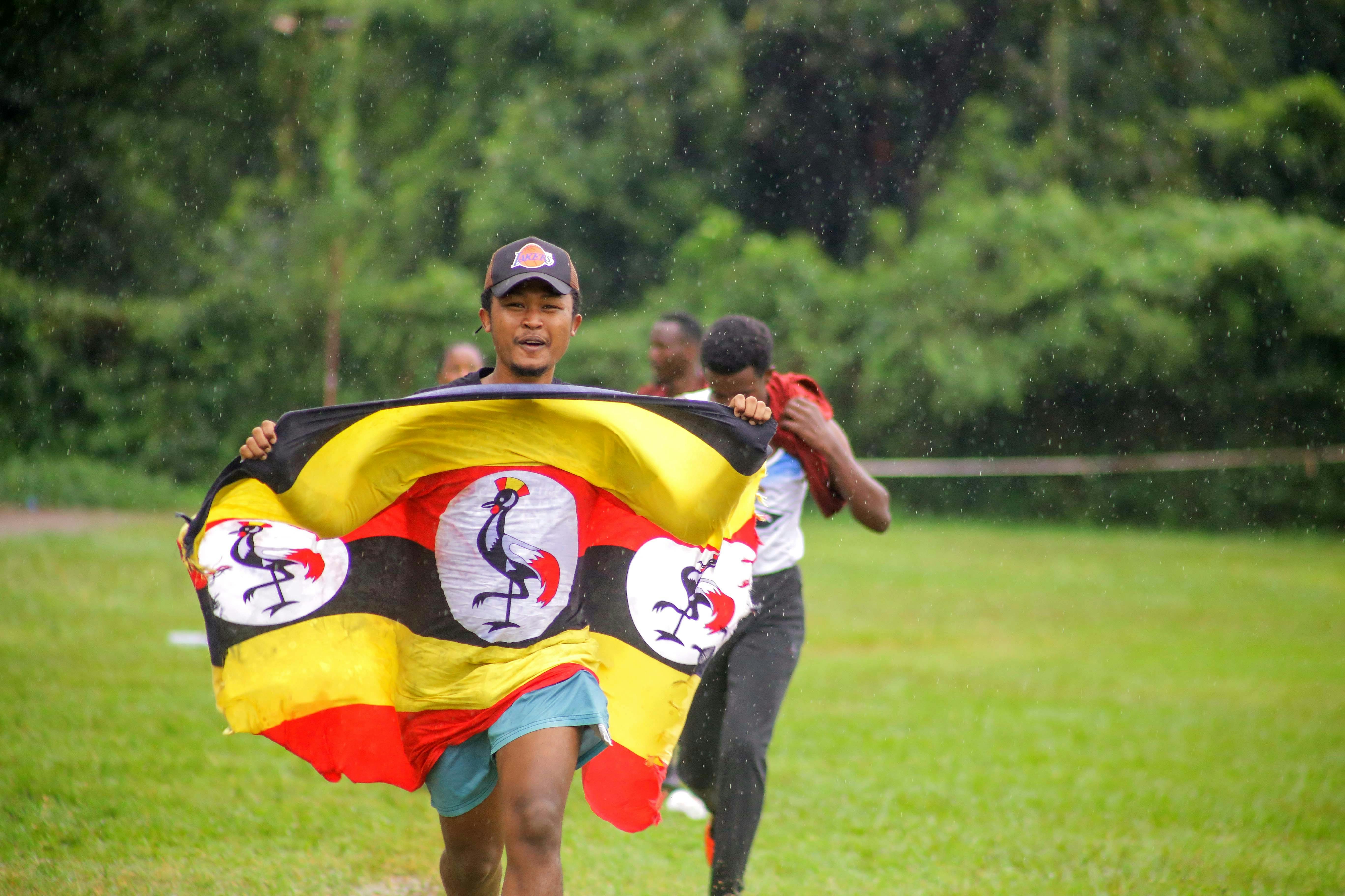Group of men running outdoors in the rain, holding a large yellow flag with red sections and white logo circles, on a grassy field.